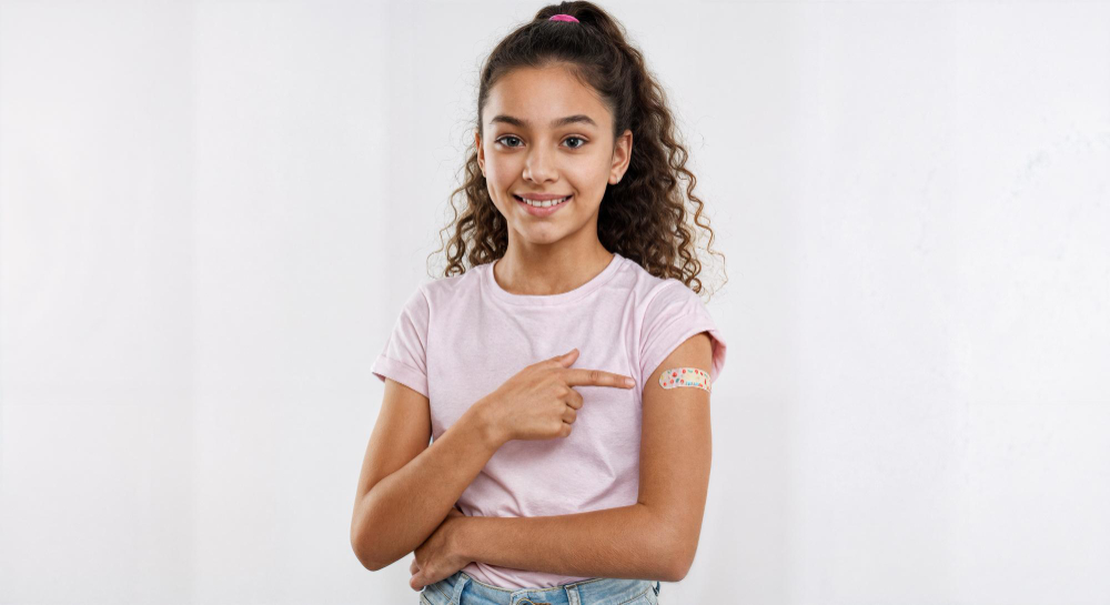 Niña sonriendo e indicando lugar de vacuna